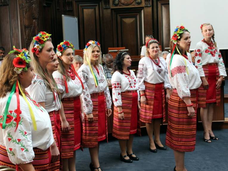 Eine Gruppe von Frauen in Folklore-Kostümen steht in zwei Reihen und singt.